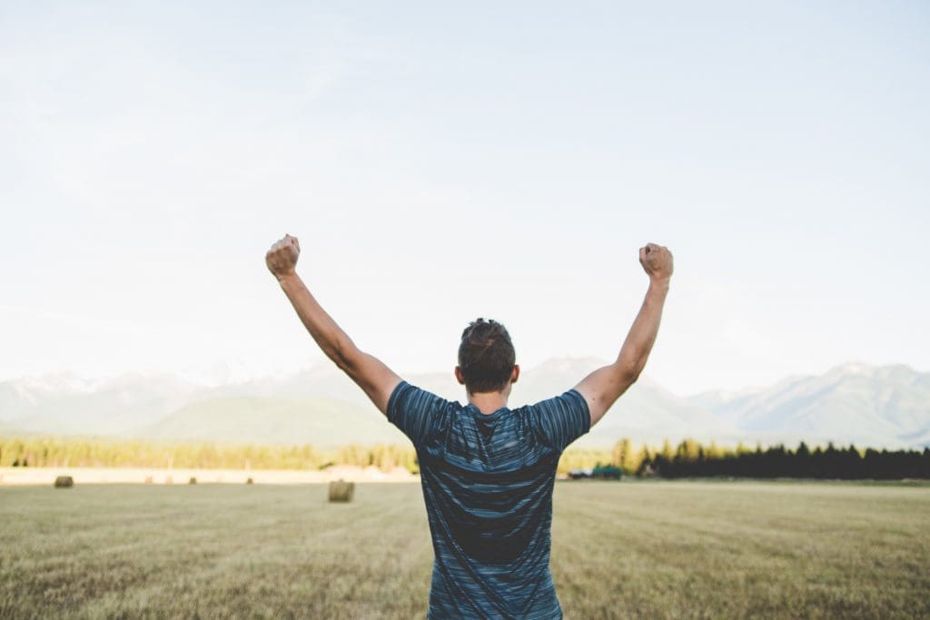 A man in a blue t-shirt stands in a field with his arms raised above his head in celebration of his reliable move in Ottawa.