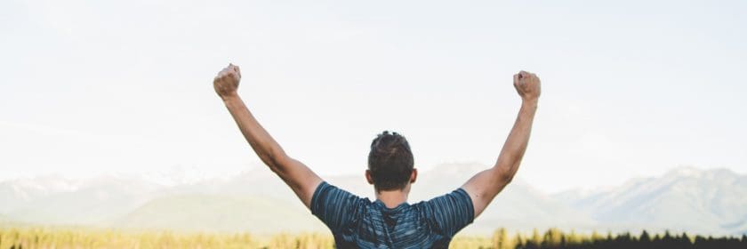 A man in a blue t-shirt stands in a field with his arms raised above his head in celebration of his reliable move in Ottawa.