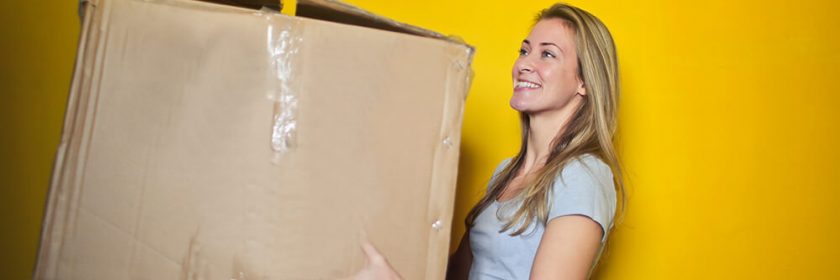 Woman in grey shirt holding brown cardboard moving box.