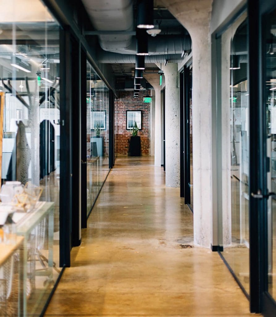 Moving Offices: What You Need to Know 3 A modern office hallway with concrete pillars and glass walls, looking towards the exit.