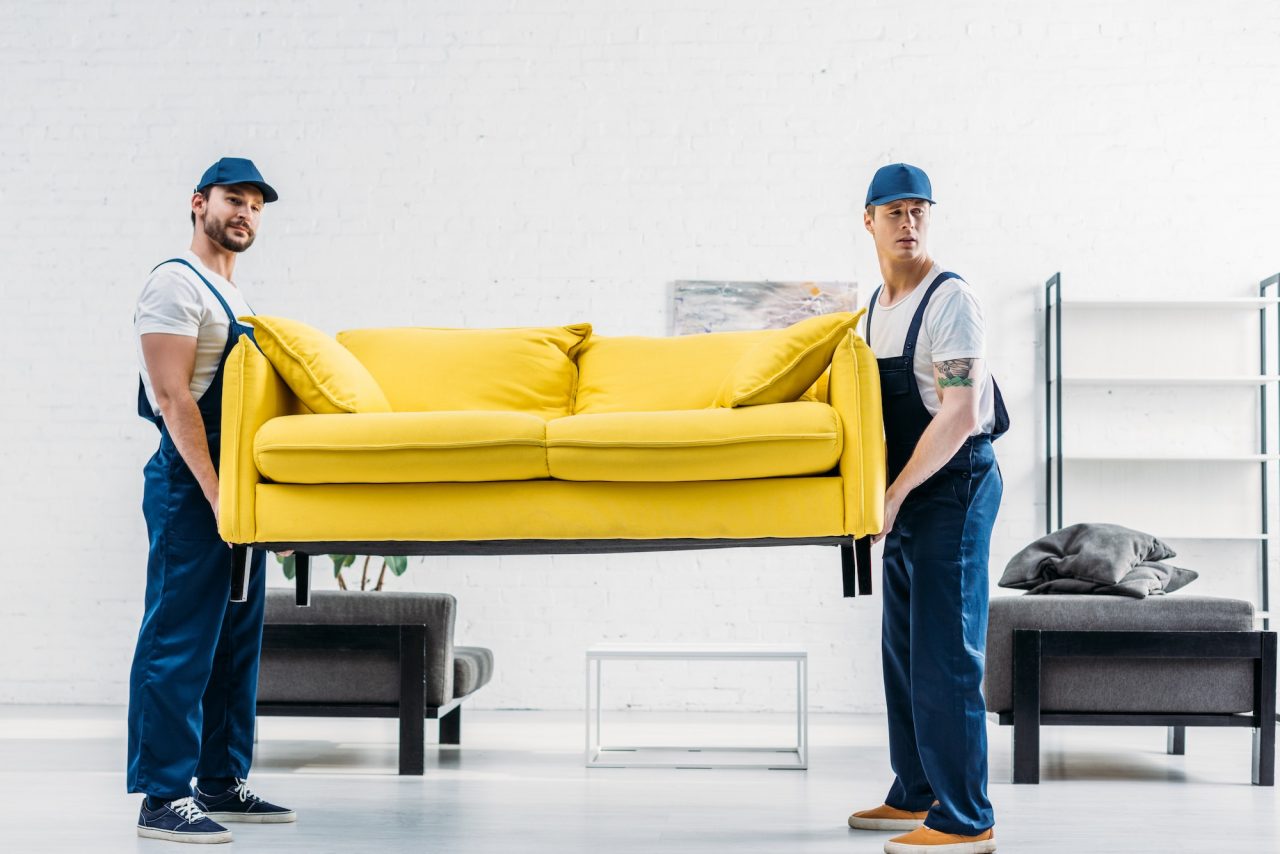 About Us 2 two movers in uniform transporting couch in apartment
